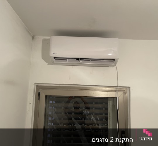 מזגן מותקן על קיר מעל חלון עם תריסים